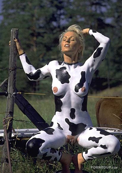 woman in cow makeup sitting naked by fence